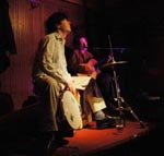 Brian sitting on a cajon at TOad during flamenco. A dark picture with an almost spotlight quality on Brian.