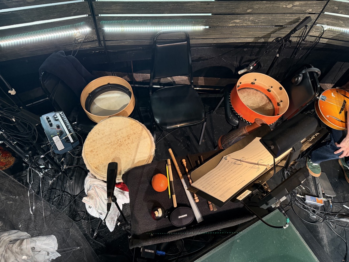 Overhead view of the Come From Away bodhr&aacute;n setup in the pit: two bodhr&aacute;ns, frame drum, djembe, tippers, brushes and a Shure microphone
